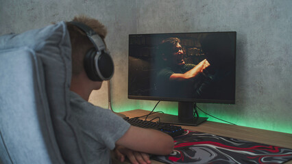 Poster - young boy wearing headphones watches online thriller movie with fight on personal computer sitting a