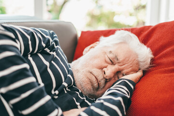 Closeup portrait of sleeping senior man with beard, peaceful grandfather resting on sofa at home, enjoying midday nap in living room. Seniors lifestyle concept