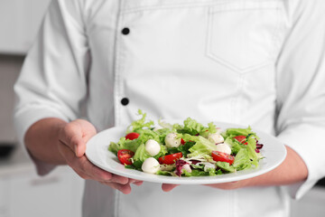 Professional chef with delicious salad in kitchen, closeup