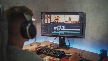 Fototapete - Teenage boy wearing headphones edits video or movie on PC. Interface of professional video editing or filmmaking software. Young film editor working remotely on freelance project on computer at home.