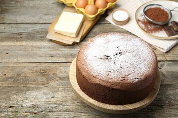 Tasty chocolate sponge cake with powdered sugar and ingredients on wooden table