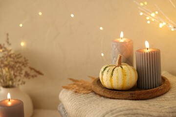 Wall Mural - Burning candles, pumpkins and stack of sweaters near beige wall, space for text. Autumn atmosphere