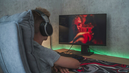 Poster - young boy wearing headphones watches online thriller movie with fight on personal computer sitting a