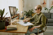 © AnnaStills - Caucasian man wearing sunglasses sitting at wooden table while listening to audio at home