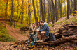 © Zoran Zeremski - Three friends resting after hiking in forest sitting on collapsed trunk and drinking tea.