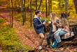 © Zoran Zeremski - Three friends resting after hiking in forest sitting on collapsed trunk and drinking tea.