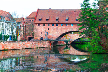  Schlayerturm tower and Kettensteg Chain Bridge over Pegnitz river in Nuremberg, Bavaria Germany. Bridge spans a river with a brick building in the background