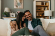 © La Famiglia - Loving modern couple sitting on the sofa, man holding a remote controller and watching a TV together