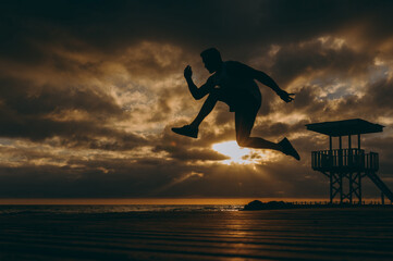 Wall Mural - Full body sideways young strong sporty athletic toned fit sportsman man wear sports clothes jump high warm up training at sunrise sun dawn over sea beach outdoor on pier seaside in summer day morning.