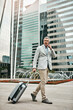 © TamJam/peopleimages.com - City, phone call and suitcase with business man outdoor, walking in parking lot of airport. Building, luggage and travel with mature employee in urban town as corporate professional for conversation