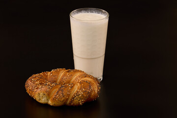 a pretzel with mixed seeds and a glass of kefir on a black background