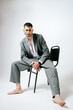 © Elina Leonova - Man in grey costume sits on the chair, barefoot. In studio, fashion