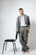 © Elina Leonova - Man in grey costume stands near the chair, barefoot. In studio, fashion
