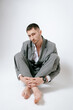 © Elina Leonova - Handsome man in grey suit sits on the floor barefoot