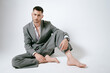 © Elina Leonova - Handsome man in grey suit sits on the floor barefoot