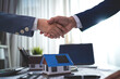 © KANGWANS - Two men shaking hands in front of a blue house. The house is a model of a house that is being sold