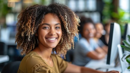 Wall Mural - A cheerful young woman with curly hair is smiling brightly while working at her computer in a modern, vibrant office space with colleagues in the background