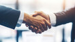 © Manatphon - Two individuals shaking hands, symbolizing agreement, partnership, or a successful business negotiation in a professional setting.
