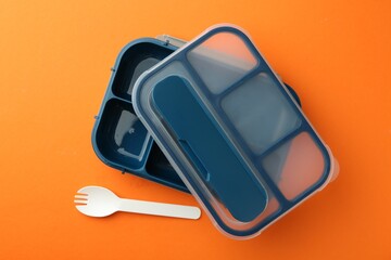 Wall Mural - Empty lunch box and fork on orange background, flat lay