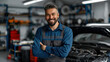 © khonkangrua - Smiling mechanic standing confidently in an auto repair workshop, with cars and tools in the background, showcasing professionalism.