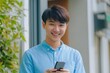 © As Sidiq - Smiling young Asian man in a blue shirt is using her smartphone to look at social media