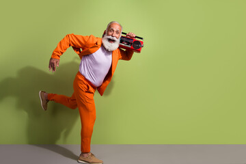 Poster - Full body profile portrait of funky eccentric grandfather hold boombox run empty space wear orange suit isolated on green color background