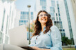 © Dusan - Young businesswoman is working on laptop in front of modern building