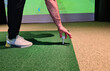 © Nadzeya - A golfer positions a golf ball on the artificial turf in an indoor facility, focusing on his grip