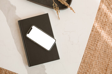 Overhead view of a mobile phone with a white isolated screen on marble table in a living room.