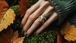 © Semiase - A hand adorned with a leaf-shaped ring rests among autumn leaves, showcasing a harmony between fashion and nature.