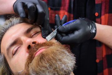 Wall Mural - Bearded man in barbershop. Hairstylist serving client at barber shop. Professional beard care. Straight razor, barber shop. Vintage barbershop, shaving. Man hairstylist. Bearded man. Closeup portrait.