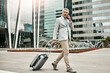 © TamJam/peopleimages.com - City, luggage and phone call with business man outdoor, walking in parking lot of airport. Building, suitcase and travel with mature employee in urban town as corporate professional for conversation