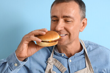 Sticker - Mature man eating tasty burger on blue background, closeup