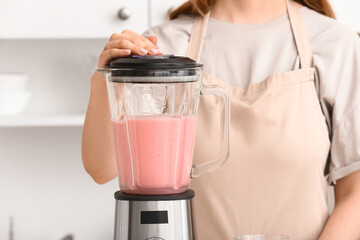 Wall Mural - Woman preparing tasty strawberry smoothie with blender in kitchen