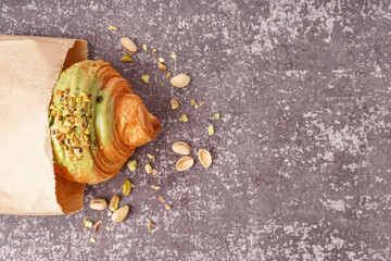 Wall Mural - Paper bag with sweet croissant and pistachio nuts on dark table