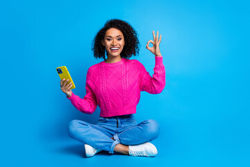 Poster - Full body photo of attractive young woman sit floor hold device okey dressed stylish pink clothes isolated on blue color background