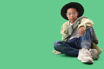 Poster - Little African-American boy in adult clothes sitting on green background