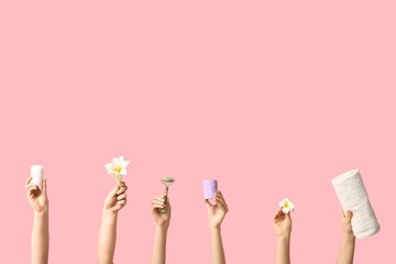 Wall Mural - Female hands with flowers, candles, towel and facial massage tool on pink background