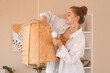 © Pixel-Shot - Young woman screwing light bulb into wicker lamp at home