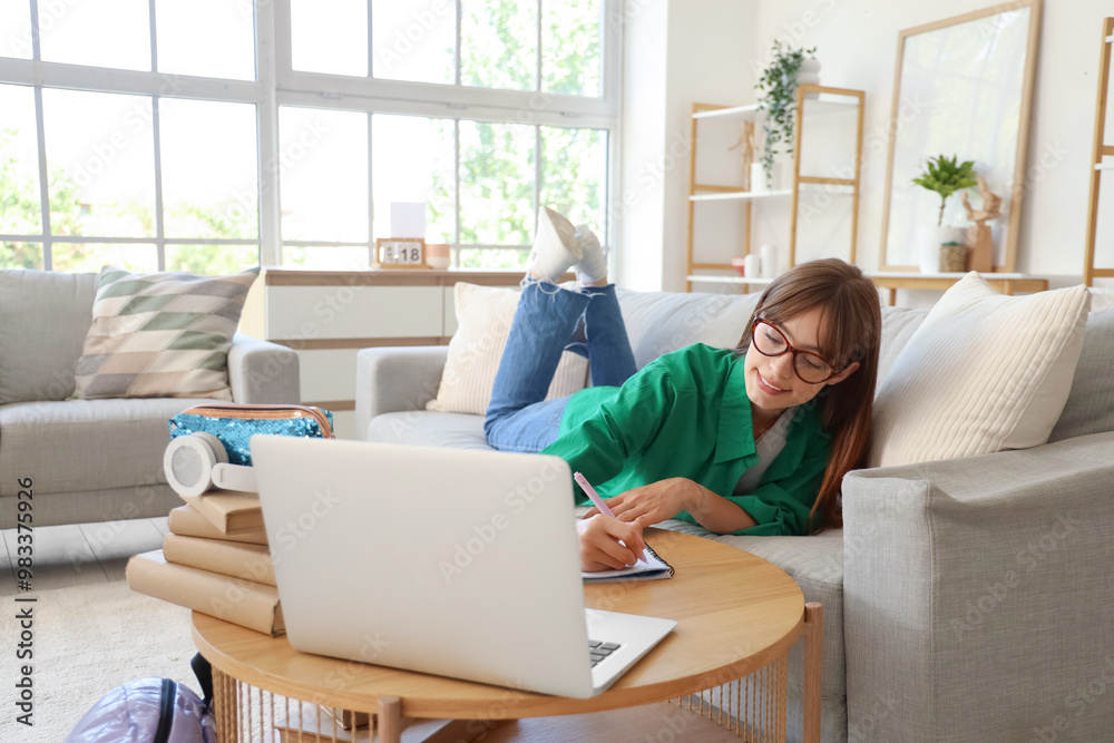 Happy female student with books and laptop writing in notebook while studying at home
