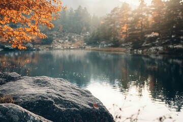 Tranquil lake with rocky shore, autumn leaves, and misty morning light in a forest setting.