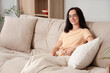 © Pixel-Shot - Young woman sitting on beige sofa at home