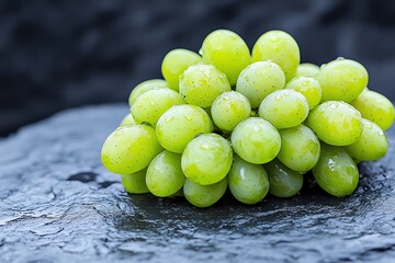 Black and green grapes with water drops, arranged on a smooth stone surface, enhancing the natural beauty of the fruit