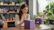 © BleizerShtorn - Smiling Woman with a Purple Gift Box and Floral Arrangement in a Cozy Home Setting