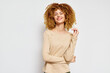© SHOTPRIME STUDIO - Smiling woman with curly hair wearing a light beige long sleeve top on a plain white background, showcasing a casual, relaxed style and confidence