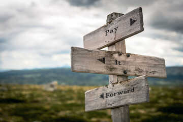 pay it forward text quote on wooden directional signpost outdoors in nature