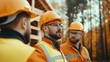 © Boontharika - Construction workers in orange safety vests and helmets discussing plans at a building site in autumn forest.
