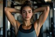 © khalid_spk - A focused young woman in athletic wear, standing in a gym with her arms behind her head