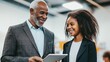 © Trushchenko_O - A man and a young woman are smiling at the camera. The man is holding a tablet and the woman is wearing a suit