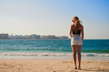 Rear view of mid adult woman strolling on beach. Traveler asian woman travel on beach in sunset. blonde-haired girl stands on the shoreline on her toes.